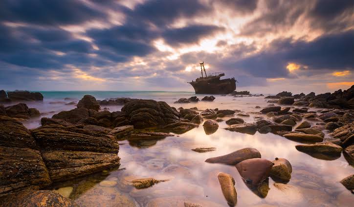 Rocky Agulhas shoreline with a shipwreck offshore at sunset