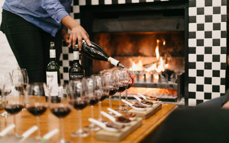 Wine being poured into tasting glasses beside a fireplace